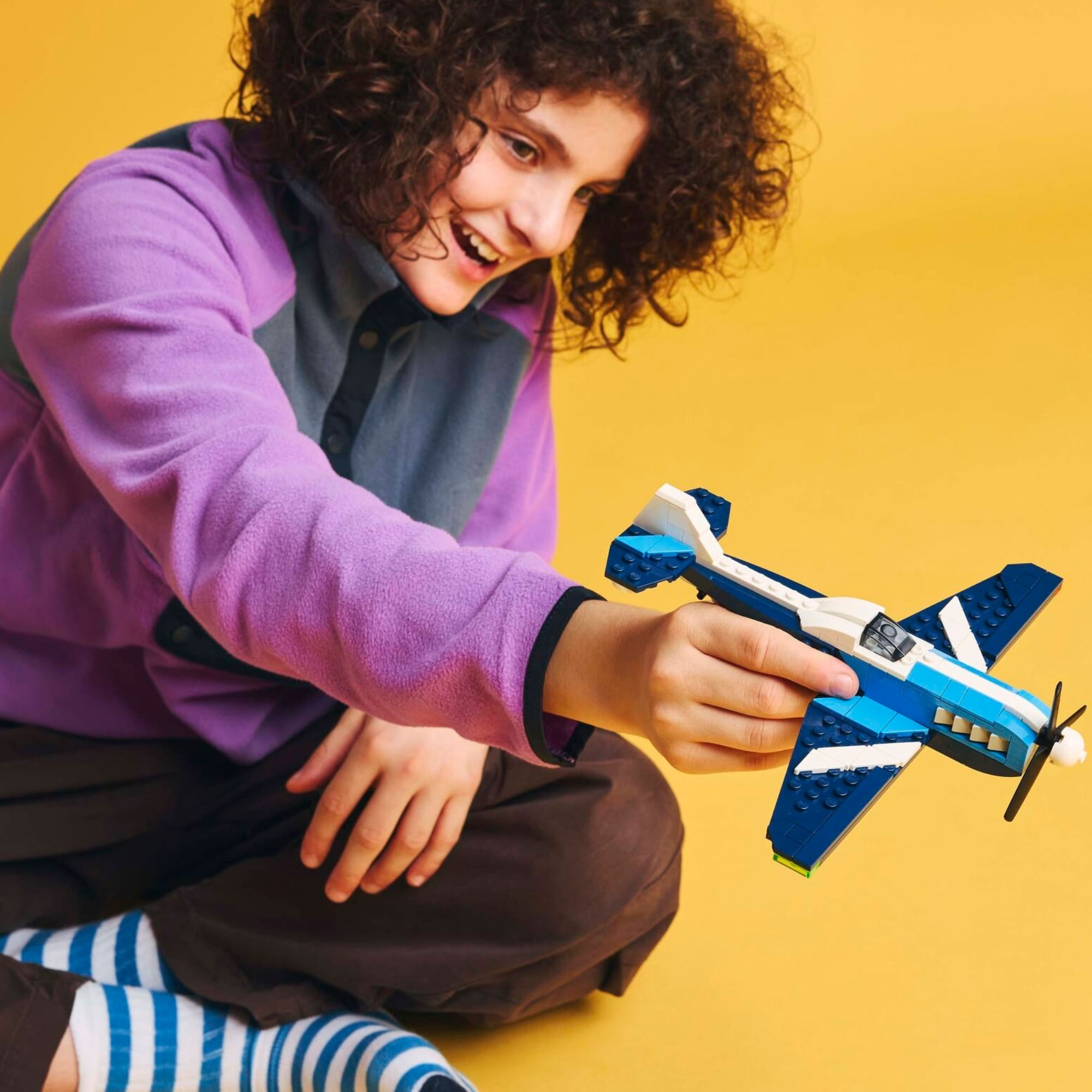Criança brincando com o LEGO Creator 31160 Avião de Corrida em fundo amarelo