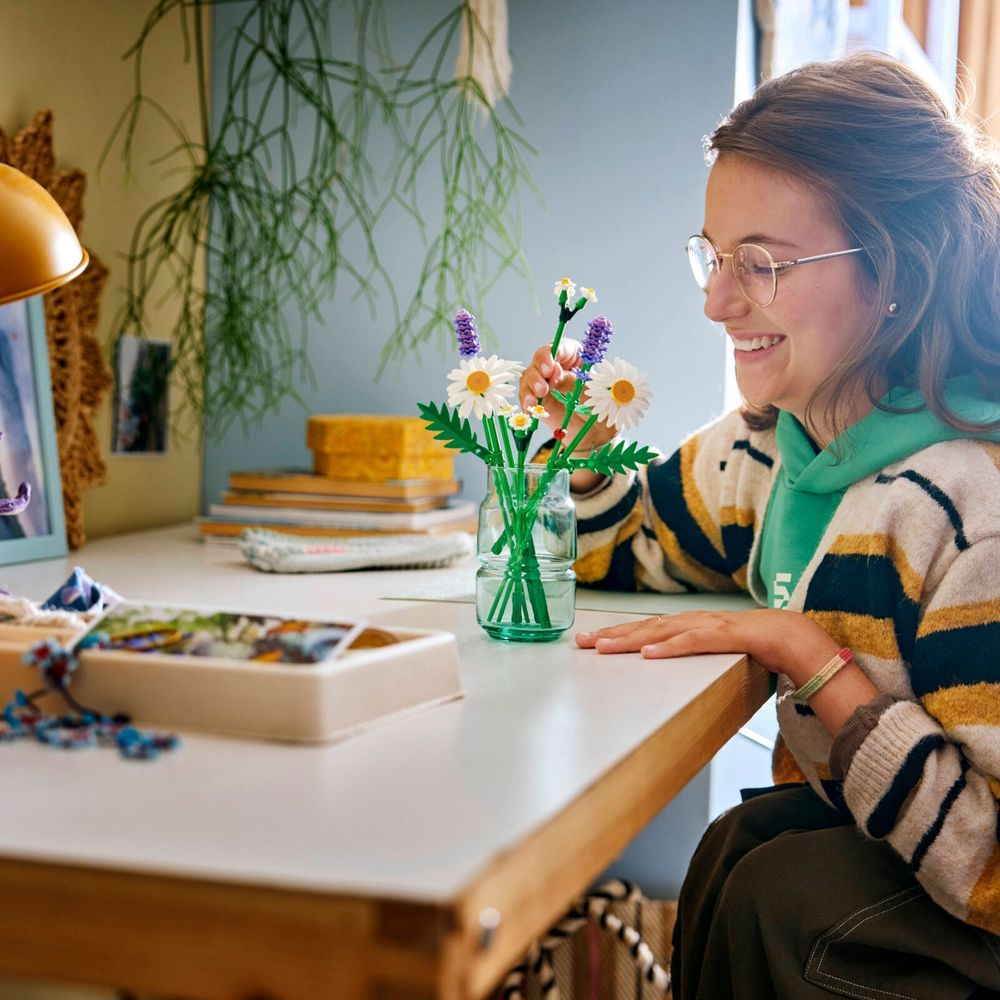 Mulher montando os Margaridas LEGO 11508 em vaso de vidro sobre mesa de jantar de madeira