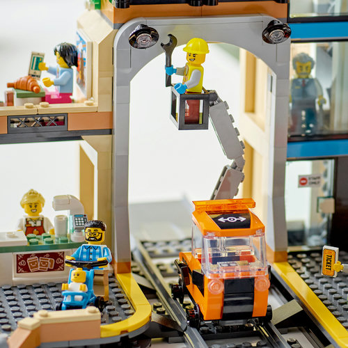 Close-up da estação LEGO 60469: operário na cesta de manutenção sobre o vagão de carga laranja