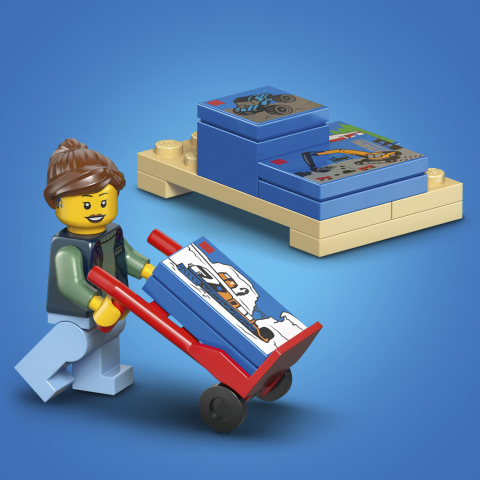 Close-up da entregadora LEGO empurrando carrinho de mão com mini caixa azul ao lado de um pallet com mais sets